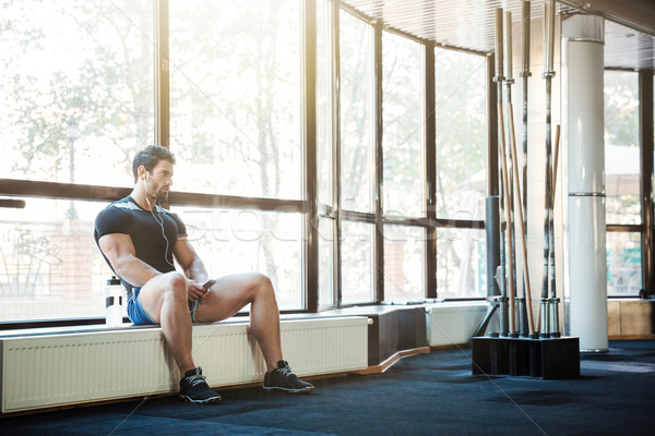 Stock photo: Sportsman listening to music sitting on windowcill