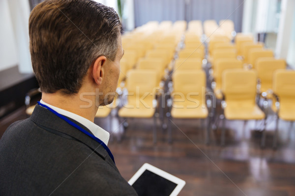 Businessman holding tablet in empty conference hall Stock photo © deandrobot