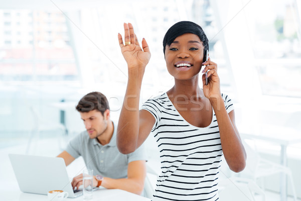 Smiling afro american businesswoman waving while talking on mobile phone Stock photo © deandrobot
