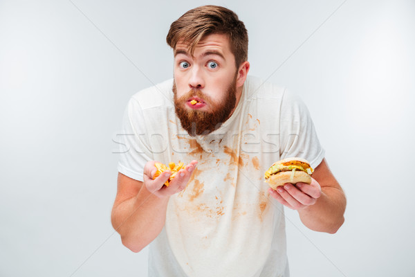 Excited hungry bearded man greedily eating hamburgers Stock photo © deandrobot