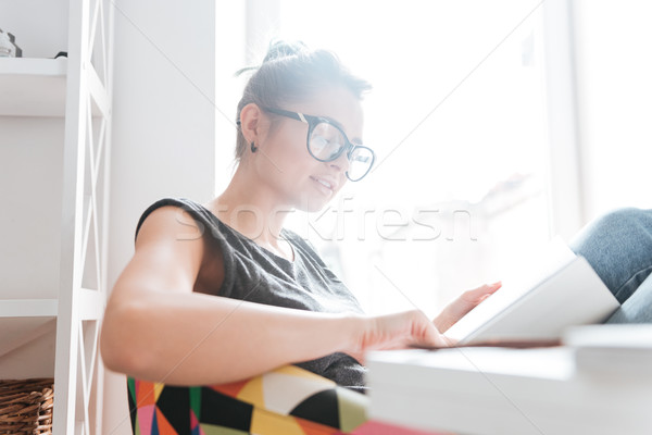 Woman in glesses sitting and reading book at home Stock photo © deandrobot