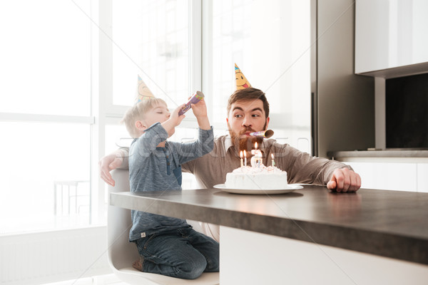 Funny father sitting near birtday cake with his little son. Stock photo © deandrobot