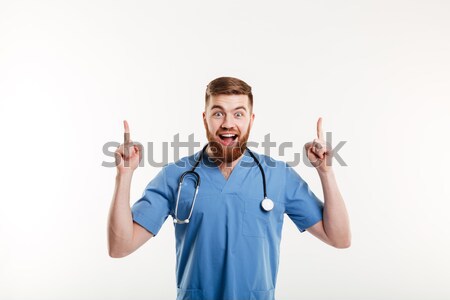Stock photo: Excited young male doctor pointing two fingers up at copyspace