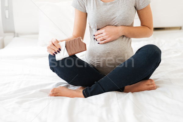 Pregnant young woman sitting and eating chocolate bar on bed Stock photo © deandrobot