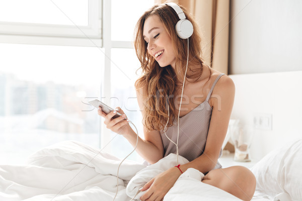 Smiling lady in pajamas listening music with smartphone and headphones Stock photo © deandrobot