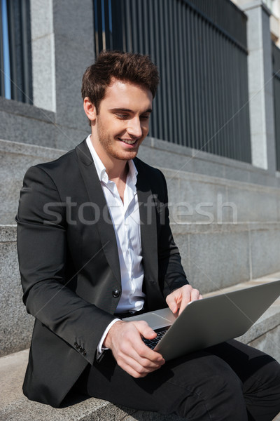 Gülen genç işadamı oturma açık havada dizüstü bilgisayar kullanıyorsanız Stok fotoğraf © deandrobot
