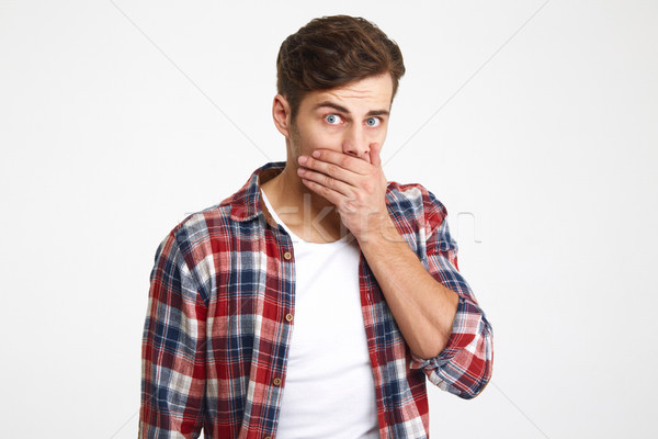 Portrait of a surprised young man covering mouth with hand Stock photo © deandrobot