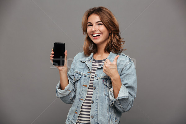 Happy young brunette woman in jeans wear showing blank mobile sc Stock photo © deandrobot