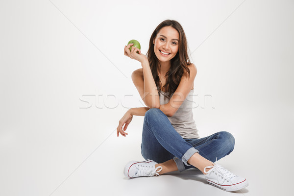 Happy brunette woman sitting on the floor with apple Stock photo © deandrobot