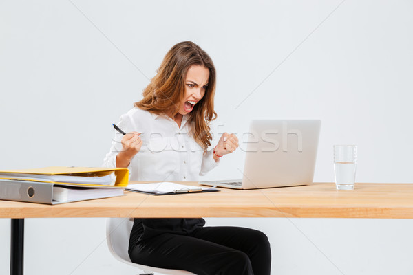 Angry young businesswoman using laptop and shouting Stock photo © deandrobot