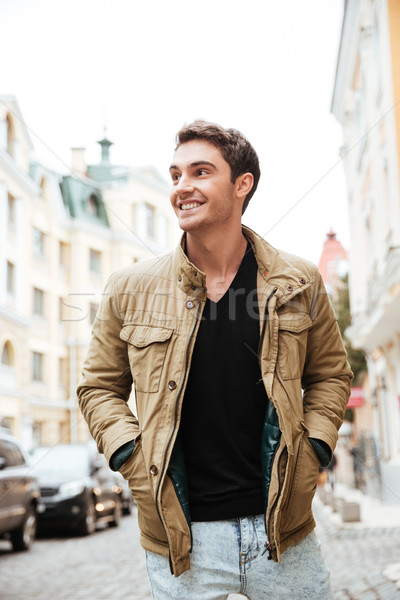 Cheerful young man walking on the street and looking aside. Stock photo © deandrobot