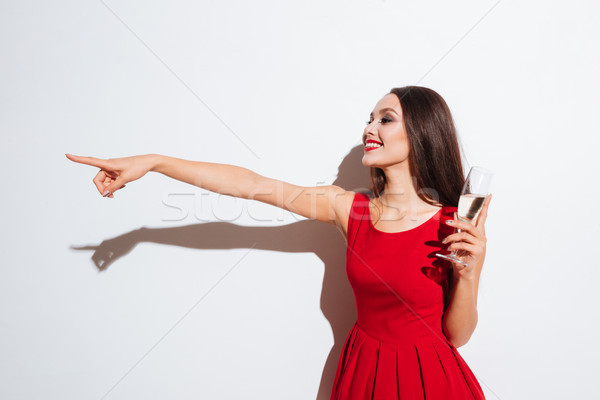 Stock photo: Smiling woman in red dress drinking champagne and pointing away