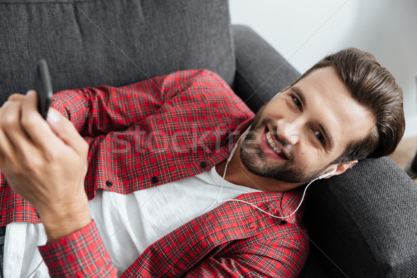 Cheerful young man lies on sofa indoors chatting by phone. Stock photo © deandrobot
