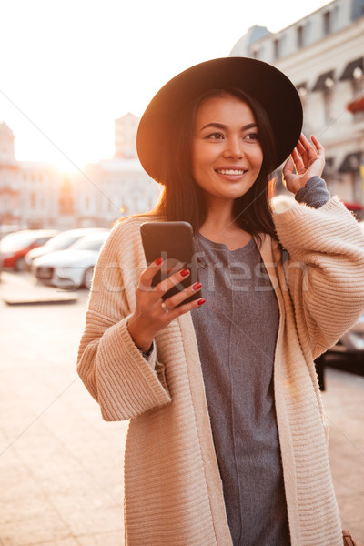 Charming trendy asian woman in black hat holding mobile phone in Stock photo © deandrobot