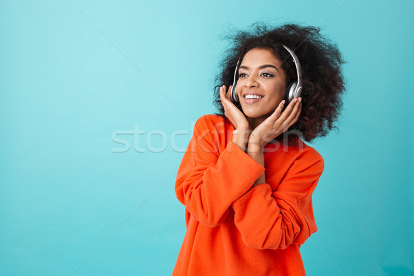 Joyous american woman in orange shirt enjoying music via wireles Stock photo © deandrobot