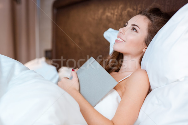 Stock photo: Young woman dreaming in her bed holding the book