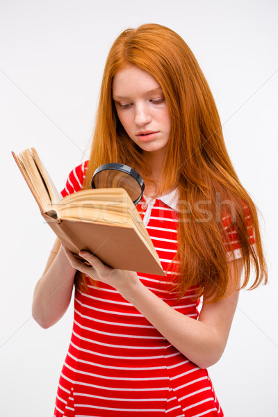 Concentrated redhead young female reading book using magnifier glass Stock photo © deandrobot