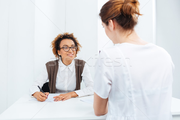 Happy african american businesswoman interviewing candidate sitting at the table Stock photo © deandrobot
