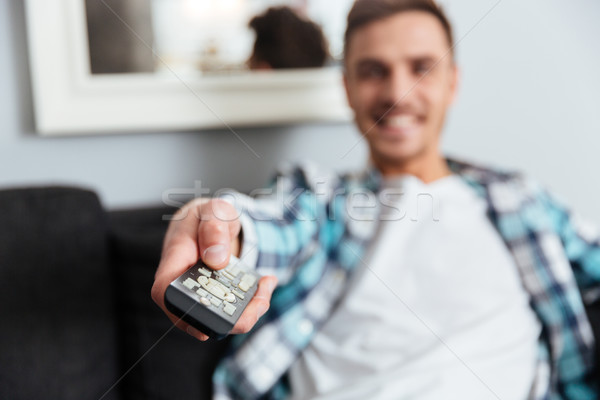 Happy young bristle holding remote control while watching TV Stock photo © deandrobot