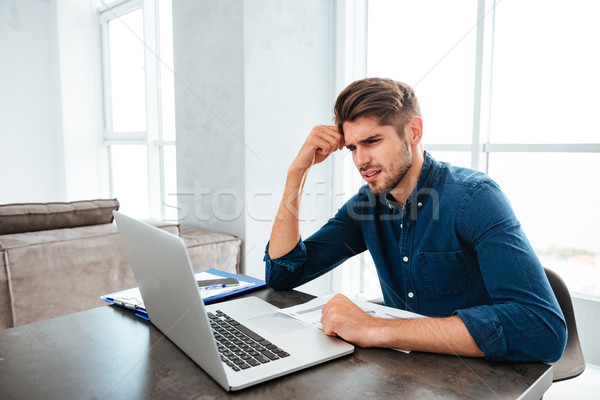 Sad young man sitting near laptop and holding head Stock photo © deandrobot
