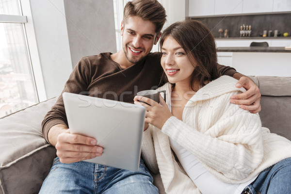 Happy couple drinking coffee and using tablet on sofa together Stock photo © deandrobot