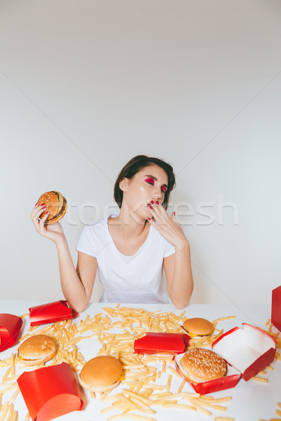 Tired young woman eating burger and yawning at the table Stock photo © deandrobot