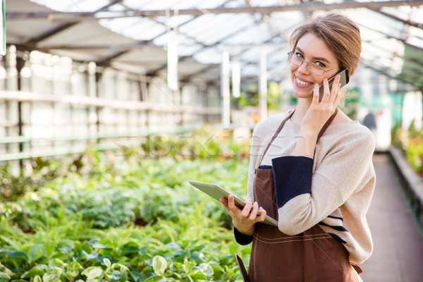 Smiling woman gardener using mobile phone and tablet in greenhouse Stock photo © deandrobot