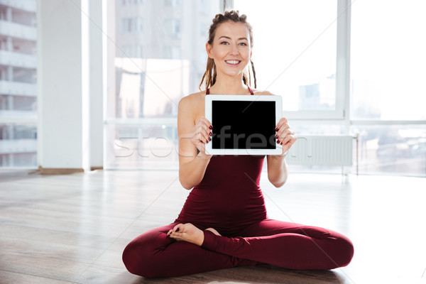 Happy woman sitting in yoga pose showing blank screen tablet Stock photo © deandrobot
