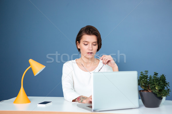 Pensive concentrated young woman sitting and working with laptop Stock photo © deandrobot