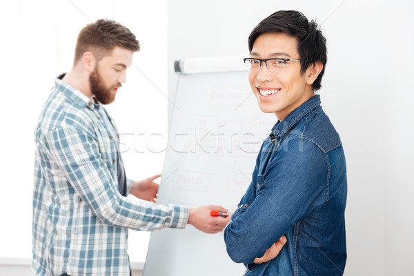 Smiling man working with his colleague using flipchart Stock photo © deandrobot