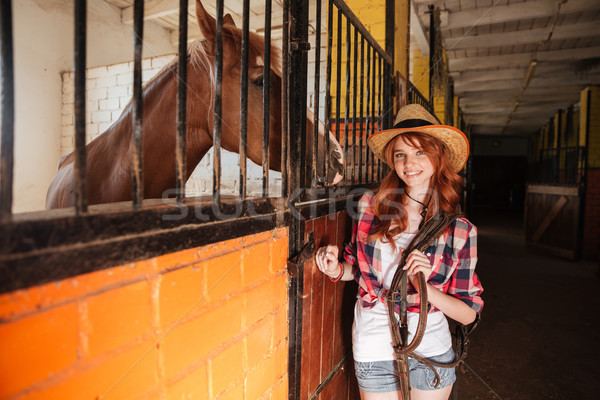 Cheerful woman cowgirl with horse standing in stable Stock photo © deandrobot