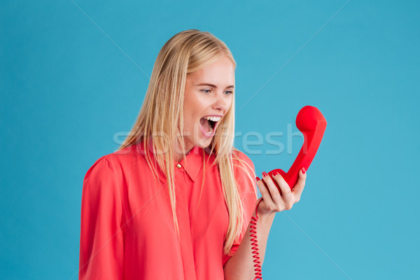 Crazy raged young female shouting in red telephone receiver Stock photo © deandrobot