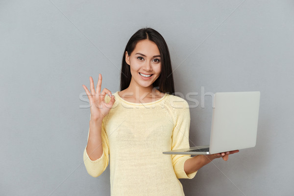 Stock photo: Woman in sweater holding laptop and showing ok sign