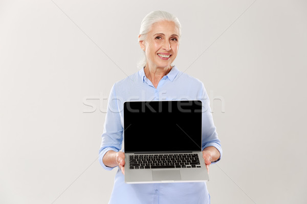 Mature grey-haired woman smiling and showing blank screen of laptop isolated Stock photo © deandrobot