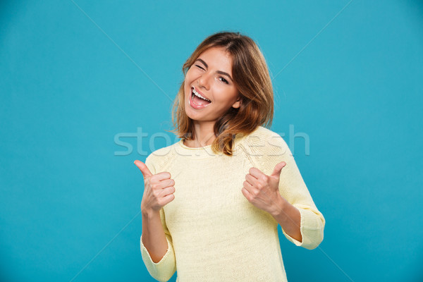 Cheerful woman in sweater showing thumbs up and winks Stock photo © deandrobot