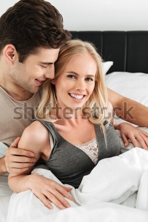 Pretty couple of smiling man and woman sitting in bed Stock photo © deandrobot