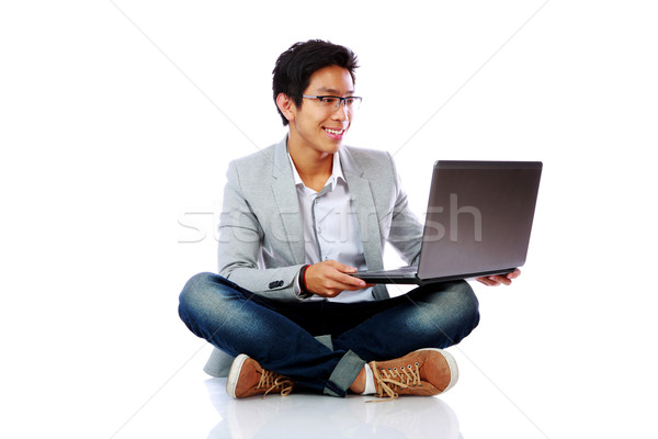 Happy asian man sitting on the floor and using laptop over white background Stock photo © deandrobot