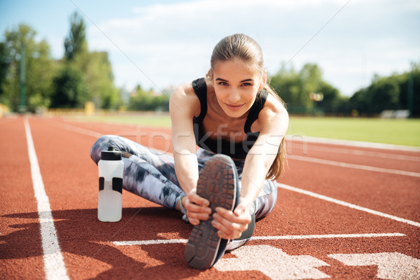 Smiling woman athlete stretching legs on stadium Stock photo © deandrobot