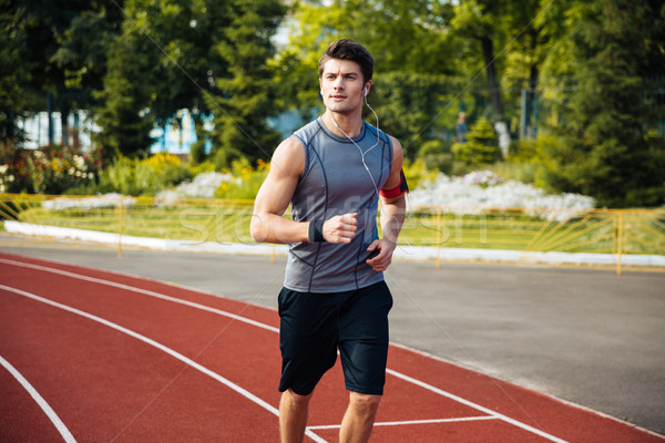 Stock photo: Young sports man running down stadium track with earphones