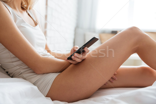 Cropped image of woman lying on bed with phone Stock photo © deandrobot