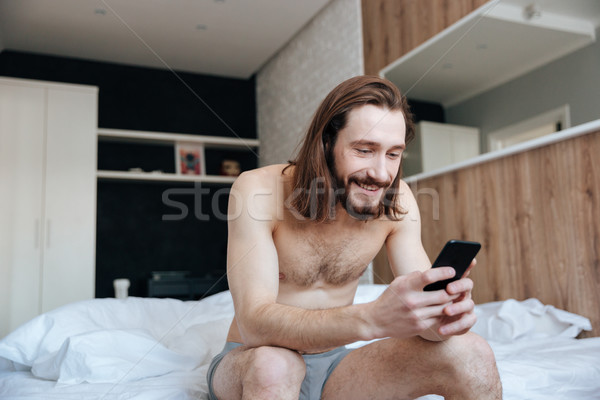 ストックフォト: 幸せ · 男 · 携帯電話 · 座って · ベッド · ベッド