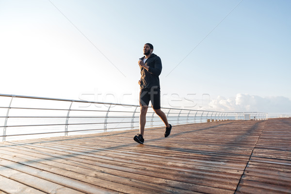 Stock photo: Sportsman listening to music and running on pier at sunset