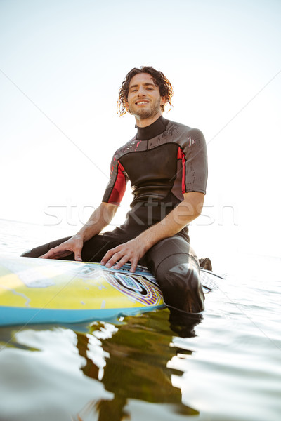 Stock photo: Surfer sitting on his surf board in water wearing swimsuit