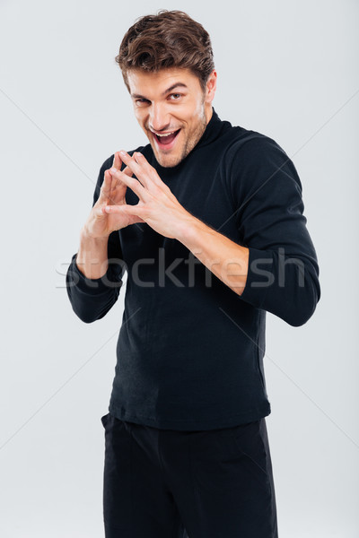 Sneaky sly young man in black clothes standing and smiling Stock photo © deandrobot