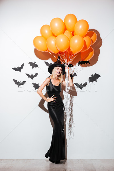 Beautiful young woman in witch halloween costume holding orange balloons Stock photo © deandrobot