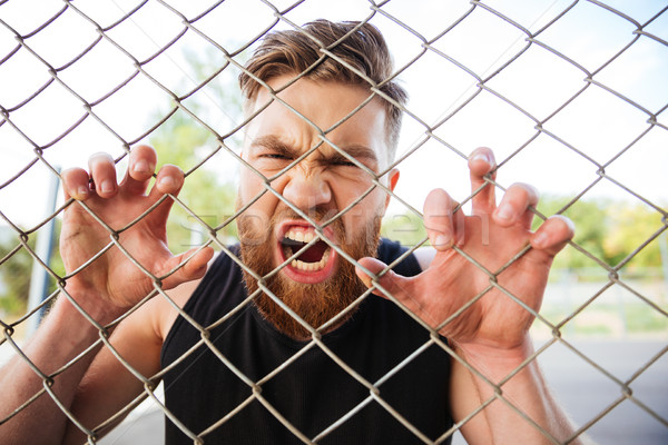 Crazy bearded man shouting with his hands on metal fence Stock photo © deandrobot