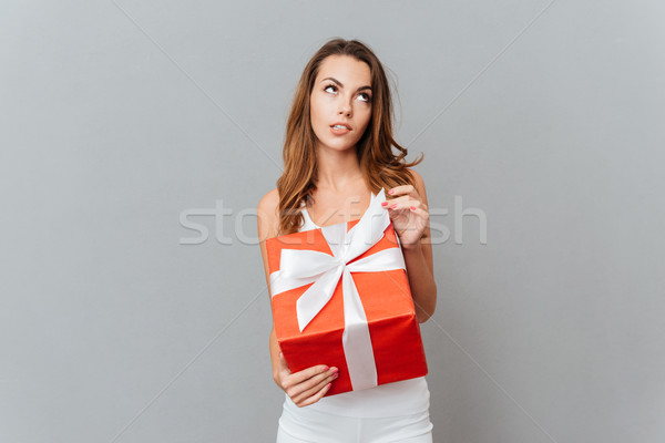 Portrait of a pensive wondered woman holding gift box Stock photo © deandrobot