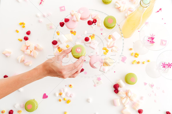 Hand taking french green macaroon from plate with desserts Stock photo © deandrobot