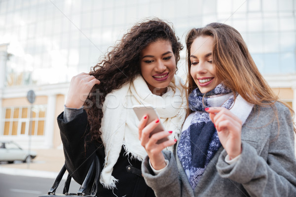 Two happy young girlfriends looking on a smartphone outdoors Stock photo © deandrobot