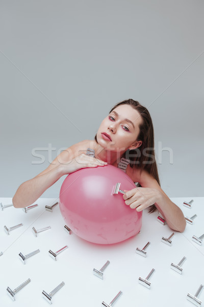 Woman sitting and applying vintage razor blade to pink balloon Stock photo © deandrobot